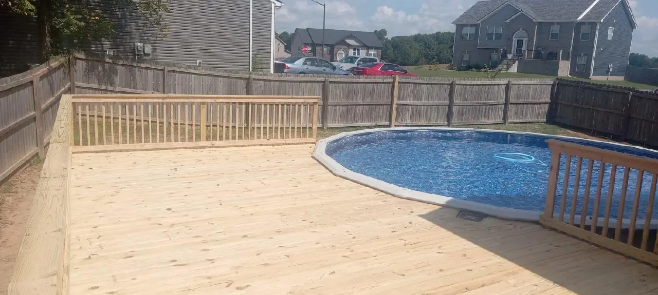 A pool with a wooden deck and fence around it.