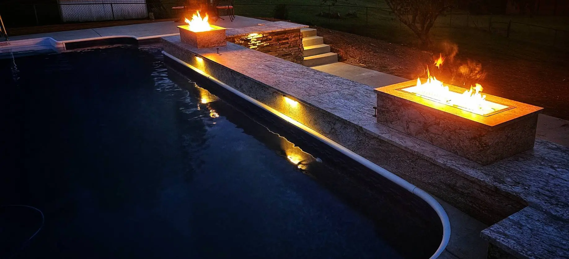 A pool with steps and fire pits in the middle of it.