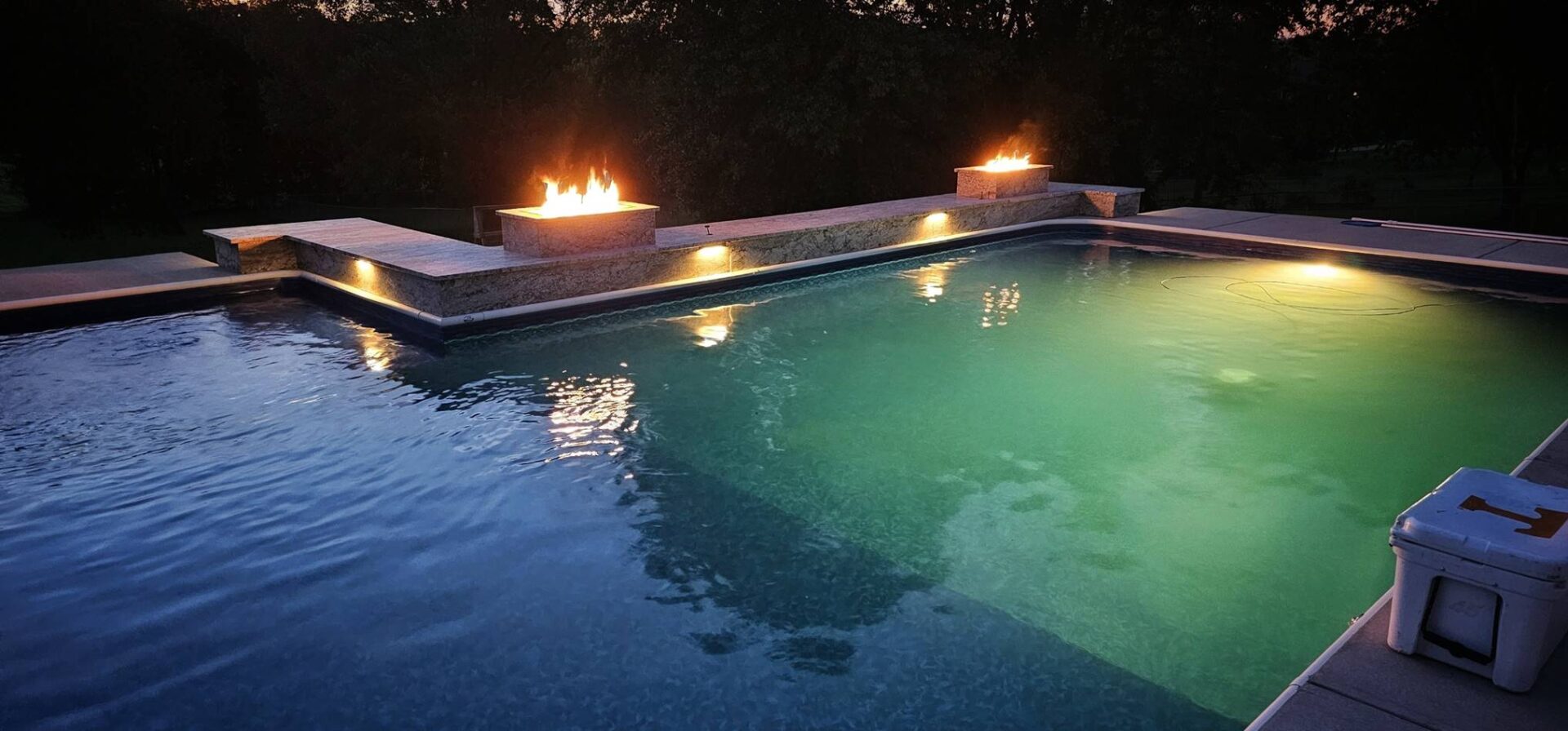 A pool with fire pits and lights on the side.