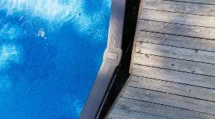 Above-ground pool edge with a gray frame bordering a wooden deck.