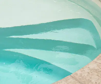 Concrete steps leading into a light blue swimming pool.