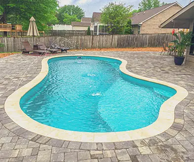 A kidney-shaped swimming pool with a stone patio in a backyard.