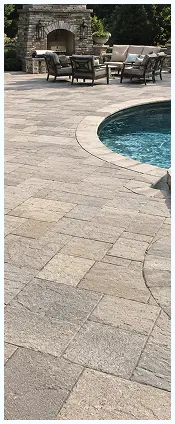 Stone patio surrounding a swimming pool with outdoor seating and a fireplace in the background.