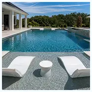 Two white lounge chairs and a small table sit on a sun shelf inside a swimming pool.