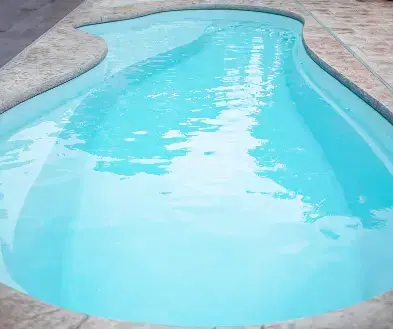 An empty kidney-shaped swimming pool with light blue water and stone coping.