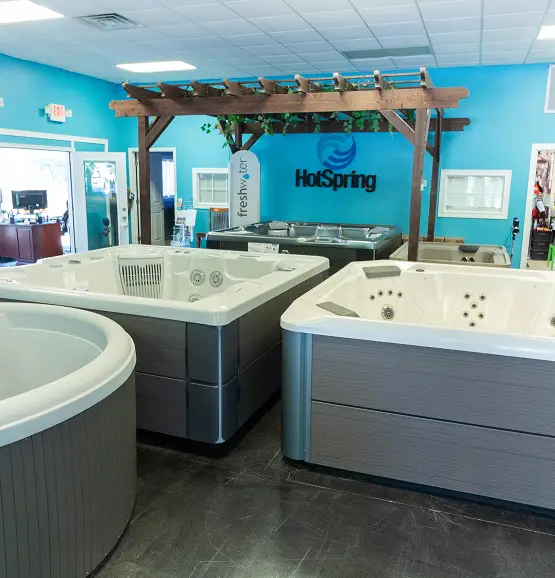 Three Hot Spring brand hot tubs displayed on a showroom floor under a wooden pergola.