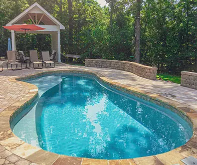 A kidney-shaped swimming pool with a stone patio, outdoor lounge chairs, and a covered pavilion.