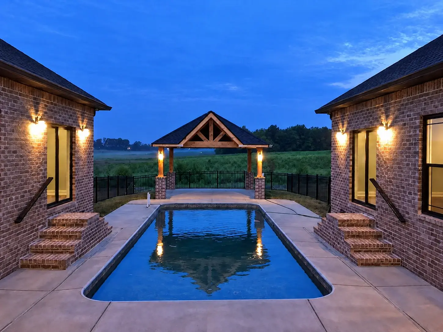 Pool at dusk facing a covered lounge and lit fire feature